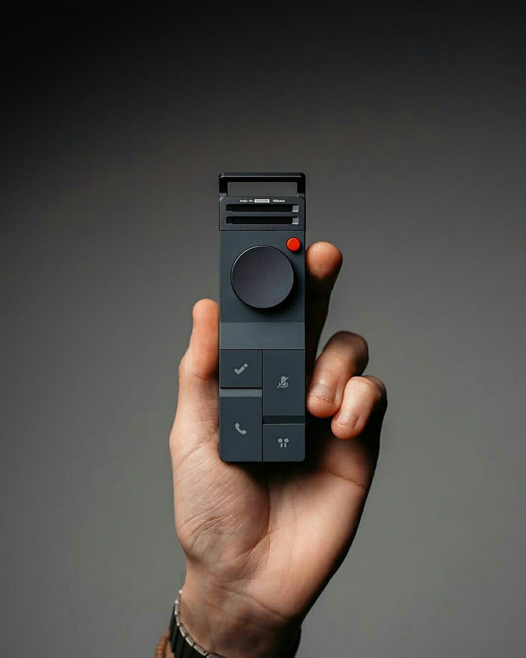 Hand holding a slate-grey push-to-talk handset with a circular dial and red accent button