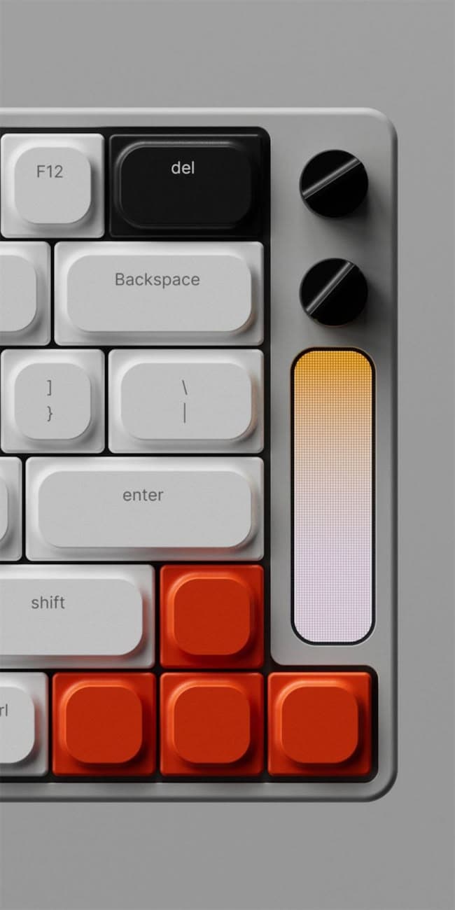 Macro of a light-grey mechanical keyboard corner with white and orange keycaps, two black knobs, and a gradient OLED strip